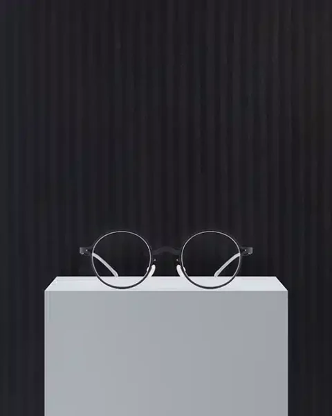 Lunettes MYKITA | Park Seo-Bo en noir Charcoal, devant une œuvre aux nuances sombres.