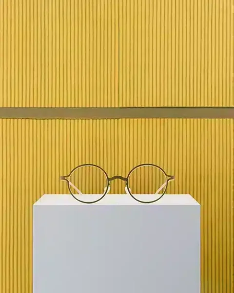 Lunettes MYKITA | Park Seo-Bo en doré Golden Olive, posées devant une toile .