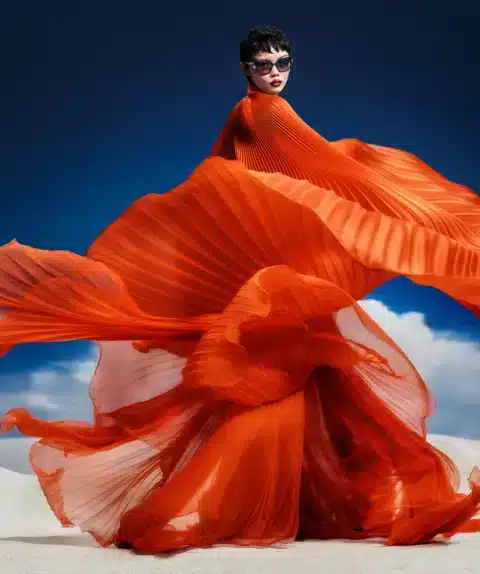 Be An Artist. Femme portant des lunettes de soleil de la collection SS25 d'Etnia Barcelona, vêtue d'une robe fluide orange dans un décor désertique.