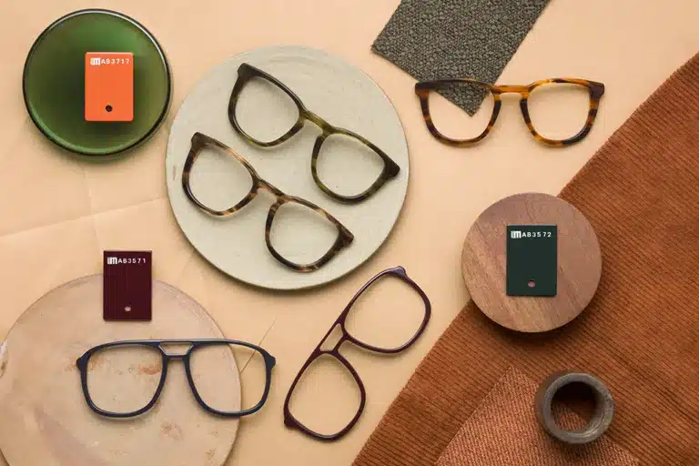 Lunettes en acétate de cellulose Mazzucchelli 1849 avec échantillons de matériaux, mettant en avant des couleurs et finitions variées sur une composition élégante et naturelle.