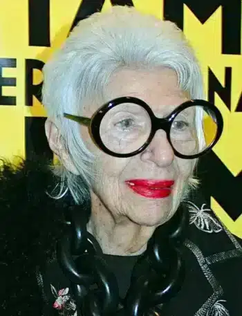Iris Apfel portant ses lunettes oversize iconiques, symbole de son style unique et excentrique.