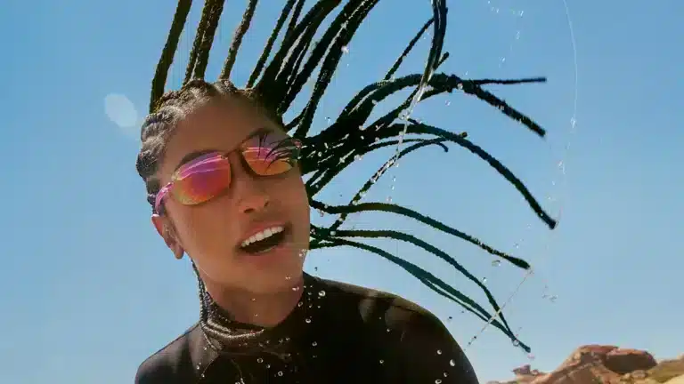 Lunettes de sport femme 2025 avec verres miroir roses portées en pleine action, cheveux en mouvement et éclaboussures sous le soleil